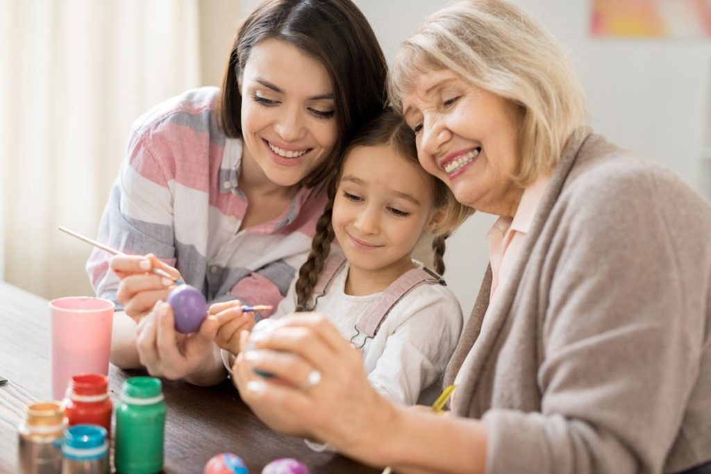 Child, mother and grandmother decorating Easter eggs in retirement village