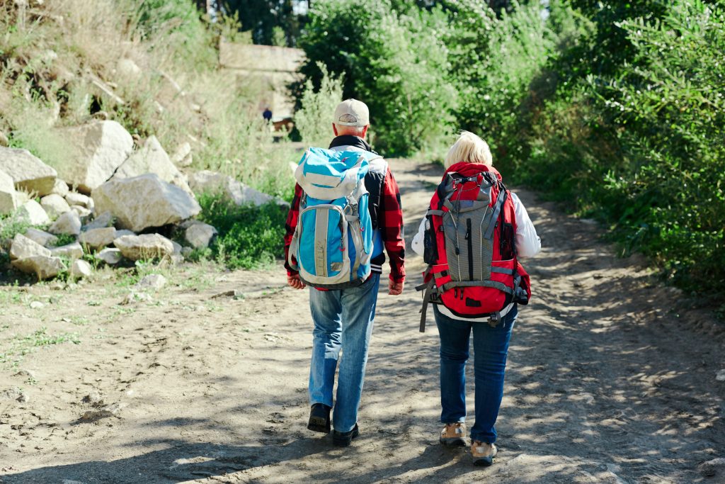 Senior backpackers walking along road by forest